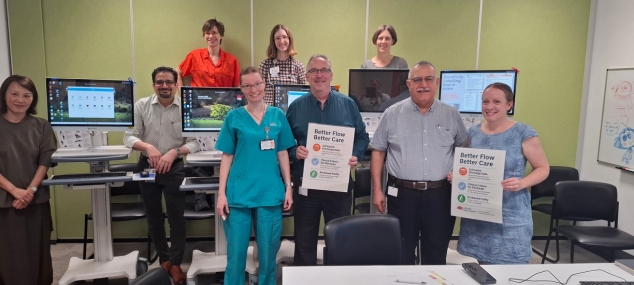 A number of admin and clinical staff standing holding Better Flow Better Care posters